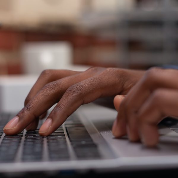 Closeup of african american hands typing business data on portable computer keyboard Closeup of african american hands typing business data on portable computer keyboard in startup brick wall office. Focus on startup employee using laptop for professional work or composing email.